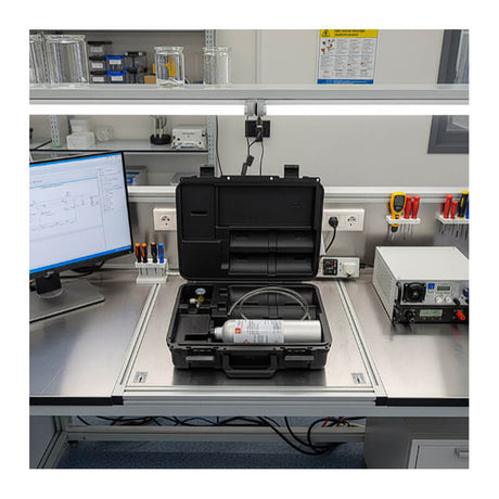 A metal lab bench with a computer, meters, and an RKI Instruments GX-3R/GX-3R Pro Calibration Kit in a black case; various laboratory equipment and glass containers are organized on shelves above.