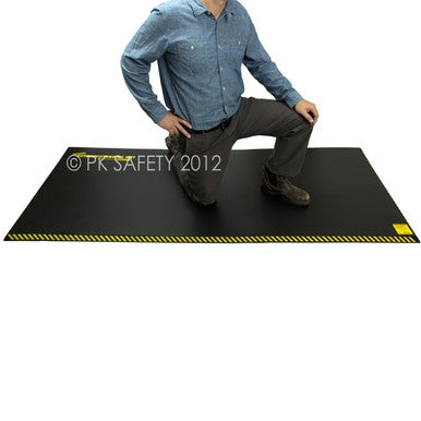 A person in a blue shirt and gray pants kneels on the Working Concepts ErgoKneel Extreme Standing Mat 5070, which features yellow-striped edges. This large black anti-fatigue mat, measuring 36 x 84 inches, is perfect for any workstation, providing comfort against the plain white backdrop.