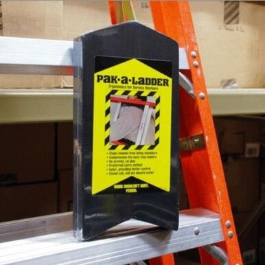 A vibrant orange ladder, the **Working Concepts Pak a Ladder 7001**, leans against a metal shelf, emphasizing the significance of safety gear. Attached to its side is a black and yellow sign from **Working Concepts** that outlines important safety guidelines. Meanwhile, brown boxes are neatly arranged on the shelf in the background.