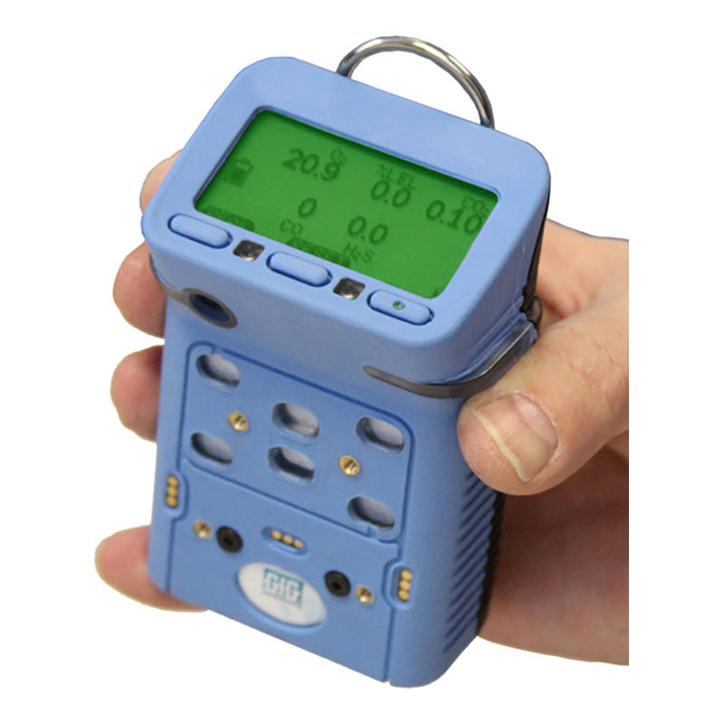 A person holds a GfG Microtector II G460 gas detector, featuring a blue casing and a green digital screen displaying numerical readings. Ideal for use in confined spaces, it offers automatic calibration, multiple buttons, and several small holes on its surface.