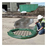 A construction worker in a safety vest and helmet installs an UltraTech Filter Sock 945_ around a storm drain on concrete, with water nearby and construction materials visible, for effective pollutant removal.
