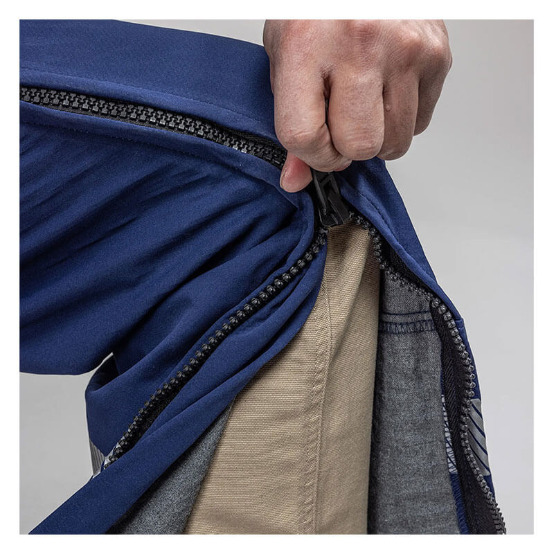 A close-up of a hand unzipping NSA’s Enespro ArcGuard Performance 40 Cal Arc Flash Bib (ARC40B), revealing beige and gray inner fabric layers. The zipper runs vertically along the side of the blue protective pants.