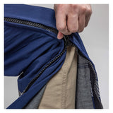 A close-up of a hand unzipping NSA’s Enespro ArcGuard Performance 40 Cal Arc Flash Bib (ARC40B), revealing beige and gray inner fabric layers. The zipper runs vertically along the side of the blue protective pants.