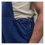 A close-up of a person wearing a beige shirt and blue NSA Enespro ArcGuard Performance 40 Cal Arc Flash Bib ARC40B, with their right hand in the pocket for arc flash protection.
