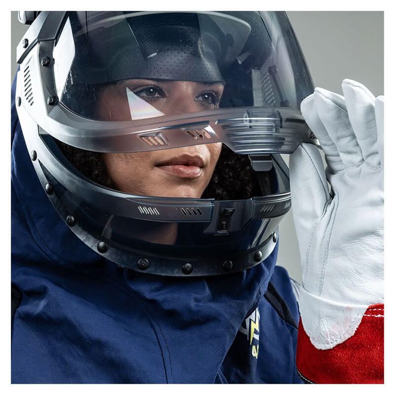 A person wearing the NSA Enespro ArcGuard Performance 40 Cal Lift Front Hood (ARC40H), along with a blue protective suit and white gloves, is shown adjusting the helmet—ideal attire for hazardous work environments.