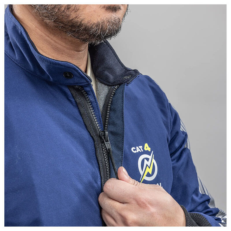 A man with a short beard zips up a blue NSA Enespro ArcGuard Performance 40 Cal Arc Flash Jacket (ARC40J) featuring a "CAT 4" logo and yellow lightning bolt on the chest. The plain background is light gray.