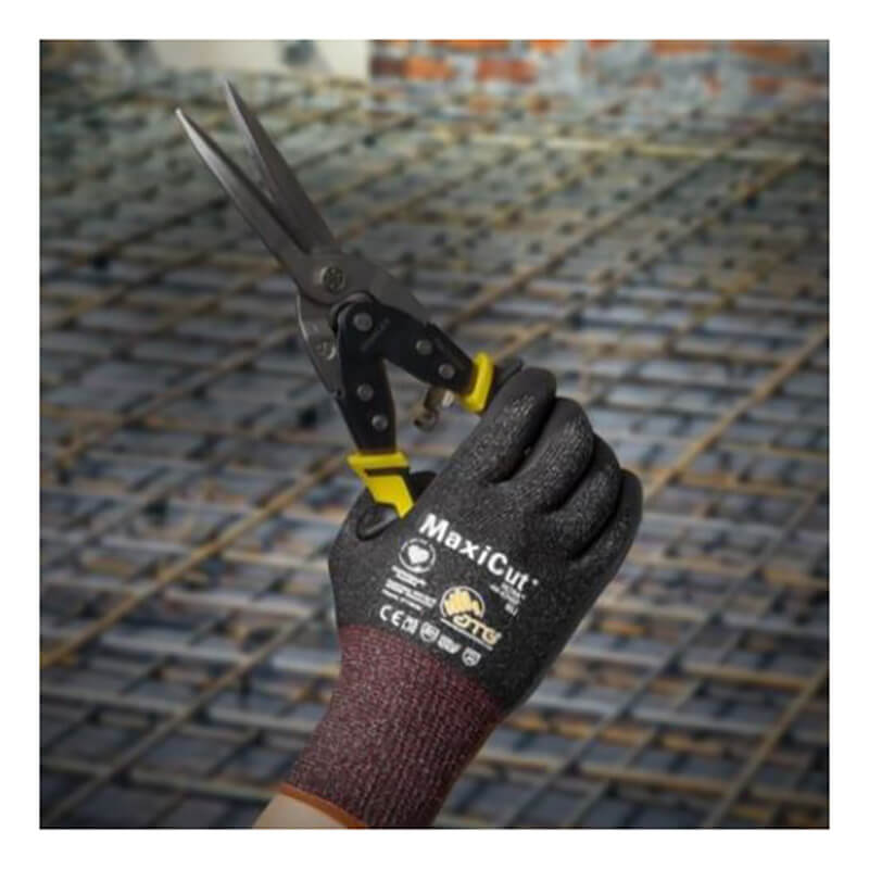 A gloved hand wearing PIP MaxiCut Ultra Nitrile MicroFoam A6 Gloves 44-6745F holds metal snips at a construction site, with steel reinforcing bars visible in the background.