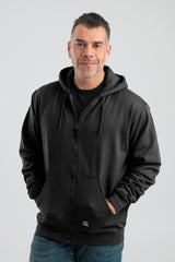 A person wearing a Berne 14 oz Black Thermal Lined Hooded Sweatshirt SZ101BK has their hands in the pockets while standing against a plain background. They have short dark hair and a slight smile, complemented by their blue jeans.