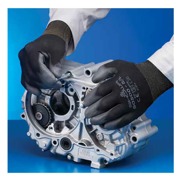 A person wearing SHOWA BO500B General Purpose Gloves by Showa Best uses a tool to work on a silver mechanical component with gears, against a blue background.
