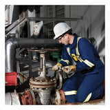 A worker in blue coveralls, safety gear, and a white hard hat uses a BW Technologies by Honeywell GasAlert MicroClip X3 4-Gas Detector MCX3-XWHM-Y-NA to inspect an outdoor industrial valve near metal pipes and machinery.