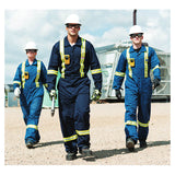 Three industrial workers in blue coveralls and vests, wearing BW Technologies by Honeywell BW Clip4 4-Gas Detector BWC4-Y-N, walk outdoors on gravel with a large wrench. Industrial equipment and a cloudy sky are seen in the background.