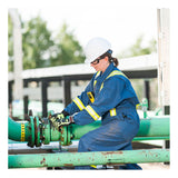 A worker in blue protective gear and a white hard hat, with a BW Technologies by Honeywell BW Clip4 4-Gas Detector BWC4-Y-N clipped on, adjusts an outdoor green industrial pipe. Trees and buildings appear in the background.