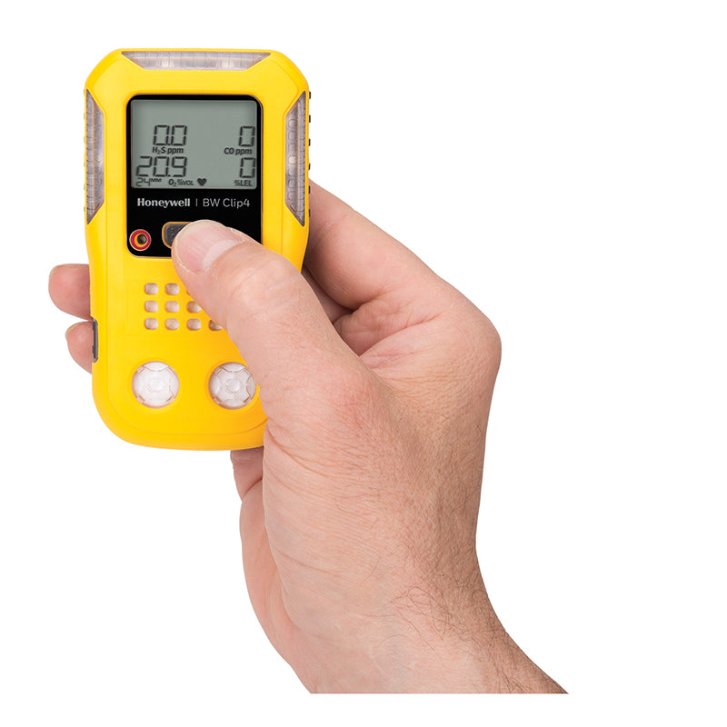 A hand holds the BW Technologies by Honeywell BW Clip4 4-Gas Detector BWC4-Y-N, with a thumb pressing a button and its digital display visible on this reliable yellow portable gas monitor.
