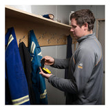 A man in a gray jacket stands by a coat rack, attaching the BW Clip Hibernation Case CLIPHB-CASE by BW Technologies by Honeywell to his belt next to blue work uniforms with reflective stripes and nearby gas monitor accessories.