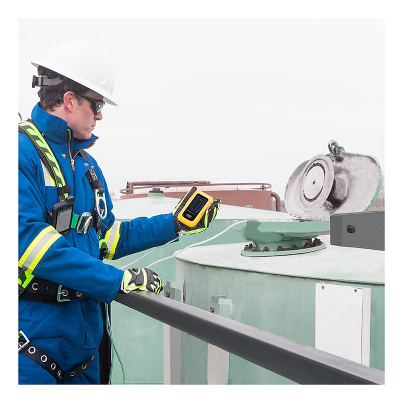 Wearing safety gear and a helmet, a worker uses the BW Technologies by Honeywell BW Ultra Five-Gas Portable Gas Detector HU-X1W1H1M1 to check readings near an open industrial tank outdoors.
