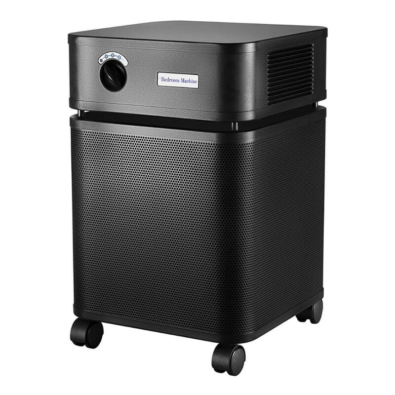 The Austin Air Systems Bedroom Machine B402 is a black, box-shaped air purifier with side vents, caster wheels, and a control dial. It uses a medical grade HEPA filter for high-level purification and has "Bedroom Machine" labeled on the front.