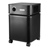 The Austin Air Systems Bedroom Machine B402 is a black, box-shaped air purifier with side vents, caster wheels, and a control dial. It uses a medical grade HEPA filter for high-level purification and has "Bedroom Machine" labeled on the front.