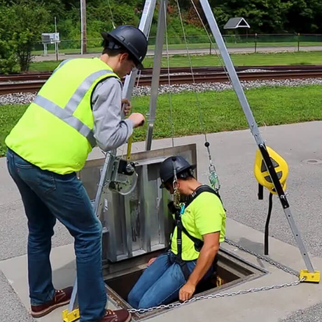 Two workers in high-visibility vests and hard hats working on a mechanical component outdoors.