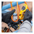 A close-up of gloved hands using the Petzl RIG Compact Descender D021_ _00 to attach an orange rope to its AUTO-LOCK system with yellow and black parts, set against a blue metal structure in the background.