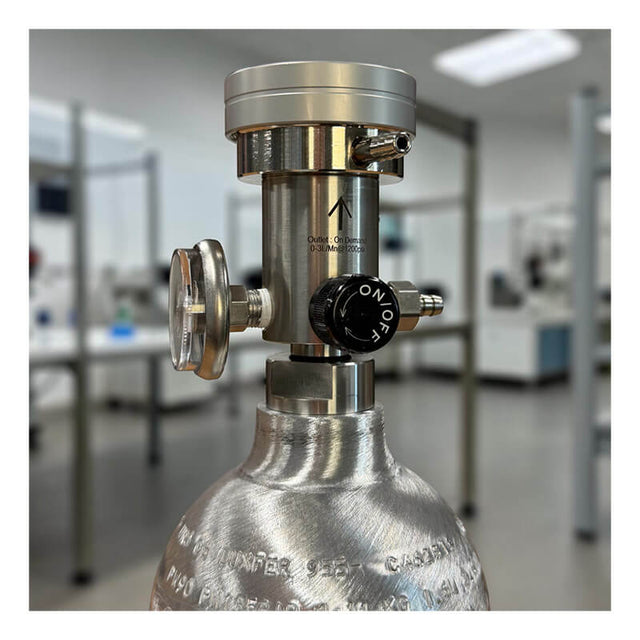 A close-up of an Intermountain Specialty Gases ISG Calibration Gas Dual Function Regulator (0-3 LPM/0.5 LPM) attached to a metal gas cylinder, featuring a pressure gauge and ON/OFF valve, set in a laboratory with blurred equipment and tables in the background.