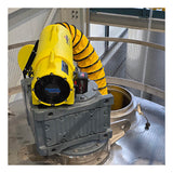 A Euramco RAMFAN UB20 18VDC industrial ventilator with a Quick-Couple Canister and flexible duct is connected to a gray metal opening on top of a large tank, delivering confined-space ventilation within the facility and enclosed by a metal safety railing.
