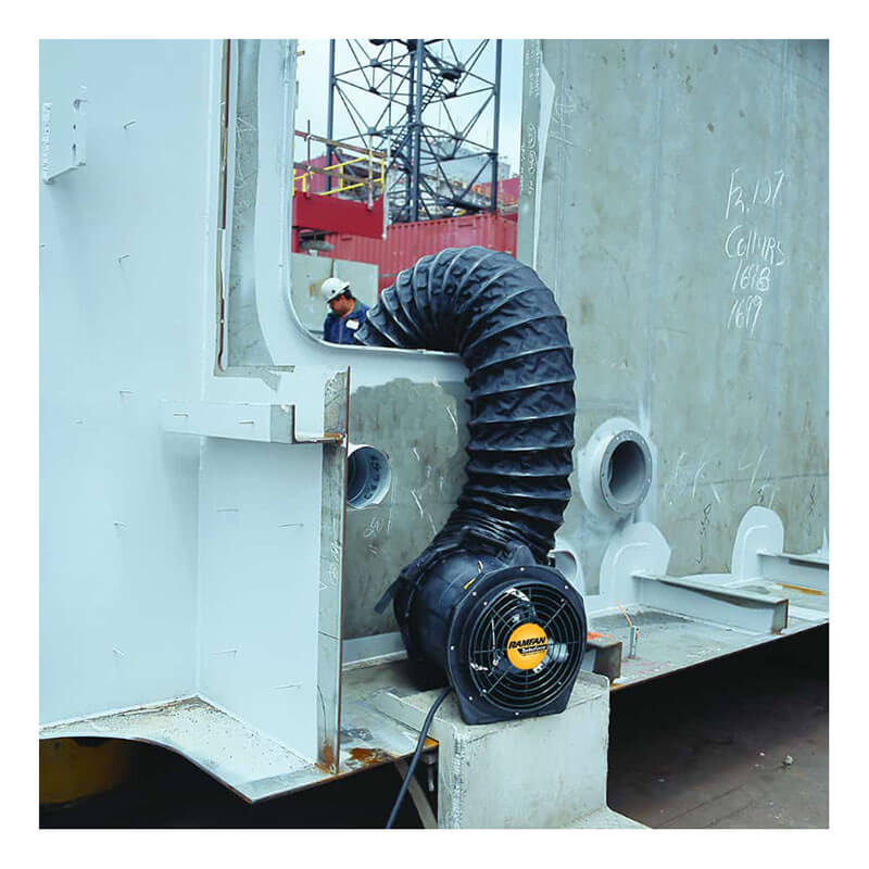 A Euramco RamFan Intrinsically Safe 12 in. Blower (EB7201XX) with a flexible black duct is set up against a metal structure, ventilating the inside, while a worker in a hard hat is visible through an opening.