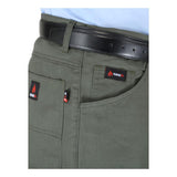 A close-up shows an individual dressed in the ForgeFR Carpenter Pants Green Duck, featuring a relaxed fit in dark green and accessorized with a black leather belt. The pants display a small red and black ForgeFR label on the pocket. This look is completed with a light blue shirt neatly tucked into these functional carpenter pants.