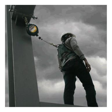 A person wearing a safety harness and hard hat stands on a steel beam against a cloudy sky, utilizing the French Creek Outlaw 30 ft SRL XR-30 from French Creek Production. Attached to a secured point, the scene emphasizes safety at an industrial site.