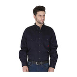 A man in a dark navy ForgeFR Forge FR Solid Button Shirt MFRLB2PS024 with chest pockets and blue jeans stands turned slightly, looking left. The FR shirt meets NFPA 2112 flame resistant clothing standards.