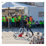 A worker in a safety vest operates equipment near a Frontline Fall Protection Patriot CS Quadpod with 3-Way Retrieval System at a construction site, while others in hard hats and high-visibility clothing observe a nearby "Caution" sign.
