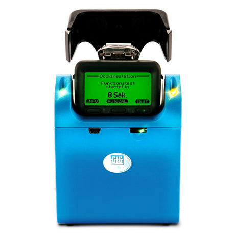 A blue electronic device resembling the GfG TS400 Test Station for G450/G460 with Charging, featuring a digital screen that reads "Dockinestation, Funktionstest startet in 8 Sek." It includes buttons labeled INFO and TEST designed for sensor diagnostics, and has a black cover open at the top.