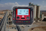 A close-up of the RKI Instruments GX-3R Pro 5 Gas Confined Space Monitor with Wireless Communication appears over an industrial plant with silos and conveyors in a dry, mountainous area. The monitor's screen displays readings for multiple gases.