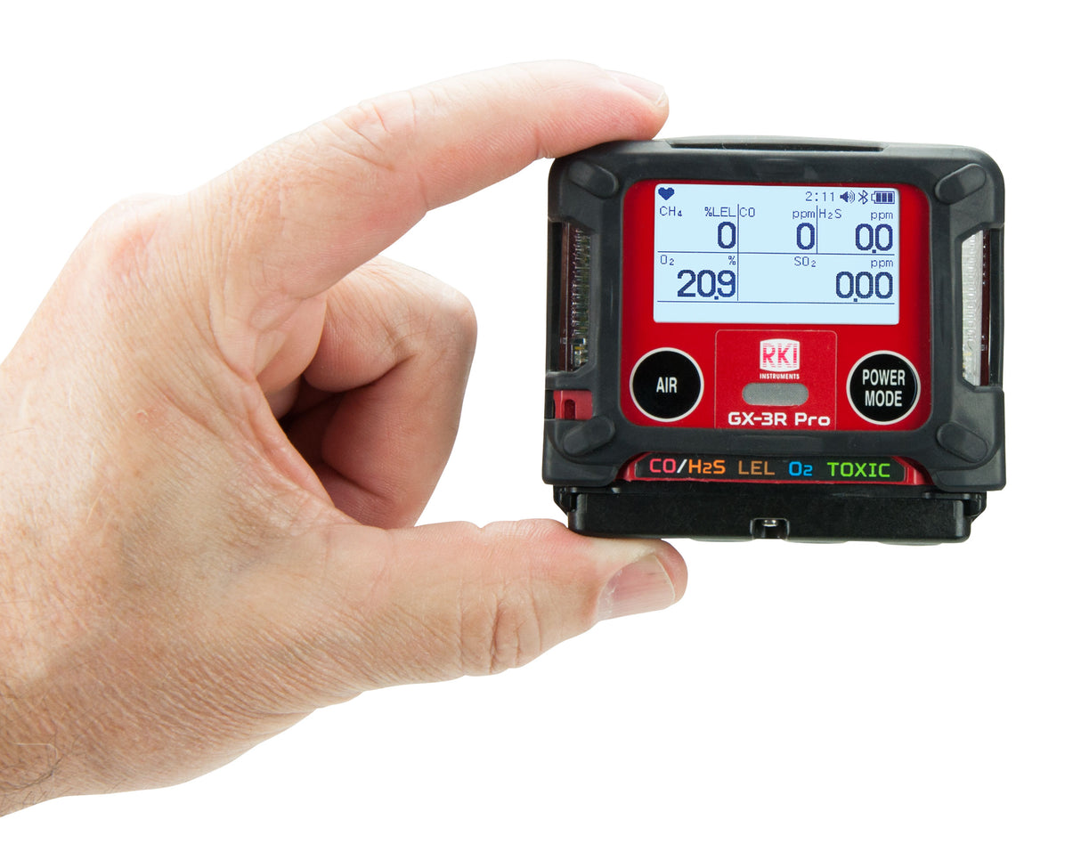 A hand holds the RKI Instruments GX-3R Pro 5 Gas Confined Space Monitor with Wireless Communication, showing digital readings for O2 and CO on a clear screen with labeled AIR and POWER MODE buttons.