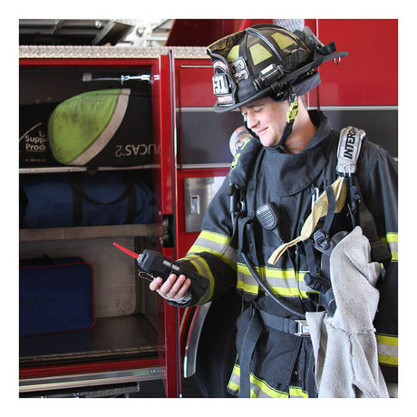A firefighter in full gear stands beside a fire truck, holding a radio and smiling. The truck’s open compartment displays equipment bags and an RKI Instruments GX-6100 4-Gas Monitor w/TC Sensor (72-61AXXT-C) inside.