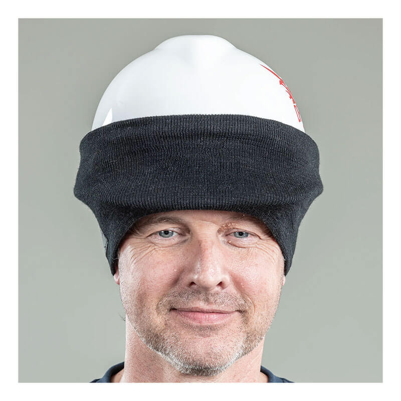A man wearing an NSA DRIFIRE FR Winter Ear Band HNCEB over a white hard hat smiles slightly against a plain gray background.