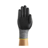 A hand wearing an Ansell HyFlex Nitrile Foam Glove 11-801, by Ansell, is shown against a white background; the glove features a black foam nitrile coating, a gray fabric wrist with a yellow cuff, and utilizes Knitted Variable Stitch Design to ensure flexibility and comfort during use.