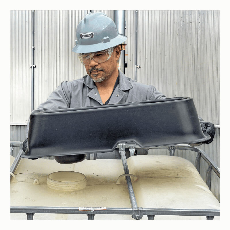A man in safety gear places an UltraTech IBC Mini Funnel 0649 onto an industrial container inside a metal-walled facility.