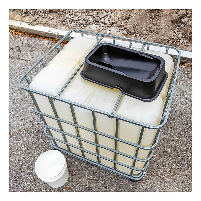 An UltraTech IBC Mini Funnel 0649 is placed on a large white plastic IBC container with a metal cage. A black rectangular basin sits on top, a white bucket is beside it, and dirt can be seen in the background.