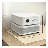 The white Austin Air "it" Machine C100 by Austin Air Systems sits on a desk mat. Measuring 8.5" tall by 11" wide and deep, it features a control knob and logo, designed to remove airborne particles and VOCs.