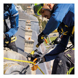 A worker in safety gear and helmet uses climbing equipment, including a Petzl ASAP'SORBER L071AB0_ energy absorber by Petzl for fall protection, while doing rooftop maintenance. Another worker’s arm is visible, with buildings and chimneys in the background.