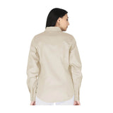 A woman with straight dark hair is shown from the back, wearing the beige ForgeFR Ladies Solid Snap Shirt LFRSLD and white pants against a plain white background, highlighting modern women’s workwear.
