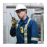 A worker in blue coveralls with PPE uses a walkie-talkie at an industrial site. A BW Honeywell GasAlert MicroClip XL Multi-Gas Monitor (MCXL-XWHM-Y-NA) by BW Technologies is clipped to his chest.