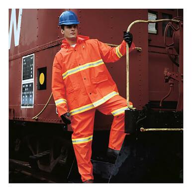 A person clad in the MCR Safety's Luminator .35mm PVC 3pc Suit 2013R, designed in high visibility rainwear with reflective stripes and compliant with ANSI/ISEA 107 standards, stands on the steps of a red train car. They wear an orange safety suit complemented by a blue helmet and black gloves while securely holding onto the railing.