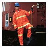 A person wearing the MCR Safety Luminator .35mm PVC 3pc Suit 2013R, featuring high visibility and reflective stripes, stands by the side of a train. Their bright orange safety attire contrasts sharply with their blue hard hat. They clutch a metal railing while stepping onto a black platform, set against the backdrop of a red train with safety markings.