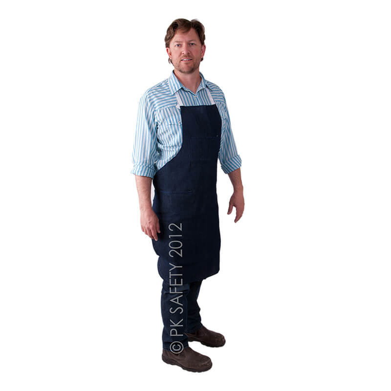 A man wearing a striped shirt and the MCR Safety Denim Apron stands against a white background. He has short hair and is dressed in dark pants and brown shoes, embodying a classic workwear style.
