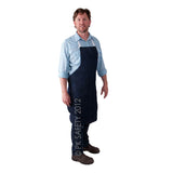 A man wearing a striped shirt and the MCR Safety Denim Apron stands against a white background. He has short hair and is dressed in dark pants and brown shoes, embodying a classic workwear style.