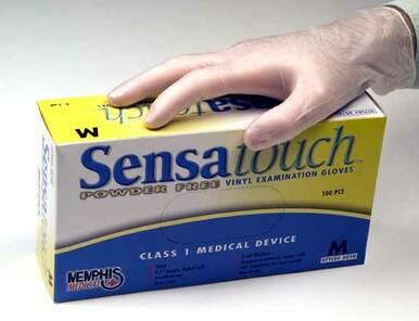 A hand wearing a safety glove rests on a box labeled "MCR Memphis Powder Free Vinyl 5010," containing 100 powder-free disposable vinyl gloves. The primarily yellow and white box indicates that these gloves, from the brand MCR Safety, are Class 1 medical devices in size M.