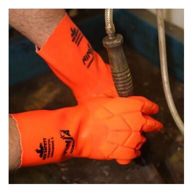 A person wearing the MCR Safety Ninja Alchemy Glove N2658HVO, showcasing its bright orange color, TPR protection, and logos, holds a tool while likely engaged in a work or safety-related task.