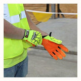 A person wearing a hi-vis vest is adjusting a pair of MCR Safety Predator Impact 1 MAXGrid Hi-Vis CutPro Gloves PD4900, which are bright orange and yellow with black protective accents, on a construction site. These gloves ensure impact resistance and offer superior Kevlar cut protection. In the background, caution tapes and construction materials are visible.