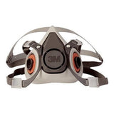 Introducing the 3M 6000 Series Half Facepiece Respirator, a gray and black mask with two round filters and adjustable straps with buckles. This respirator is NIOSH-approved for reliability, and the central 3M logo signifies its quality craftsmanship.